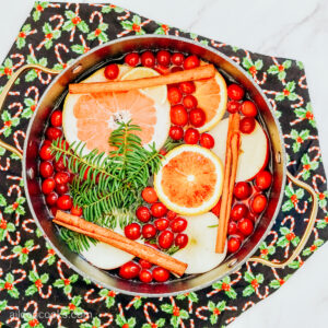 Aerial view of a simmer pot, filled with ingredients to give a holiday-themed aroma, sitting atop a holiday-themed placemat