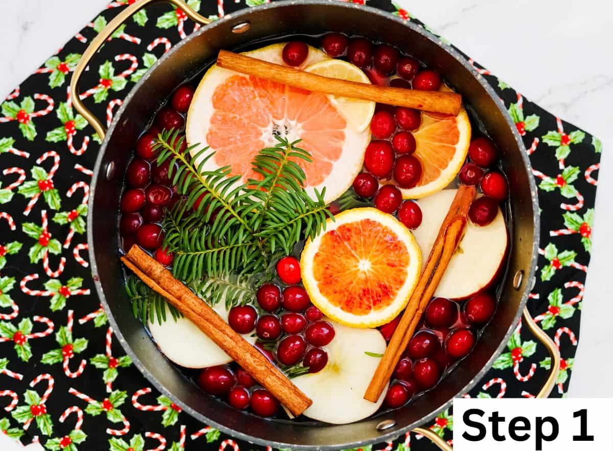 A large pot filled with orange slices, cinnamon sticks, cranberries, and rosemary sprigs.