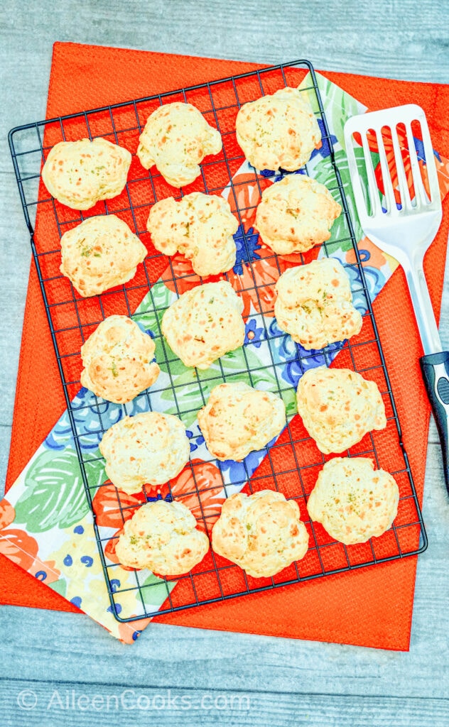 Aerial view of cheese biscuits on a black wire rack, sitting a red table cloth, with a spatula.