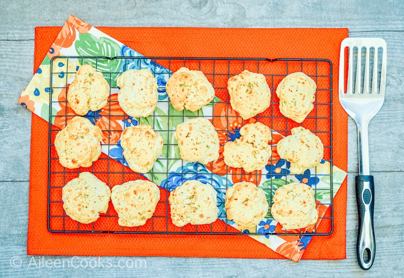 Aerial view of cheese biscuits on a black wire rack, sitting a red table cloth, with a spatula.