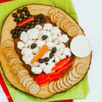 A Snowman Veggie Tray served on a wooden platter with red and green placemats in the background