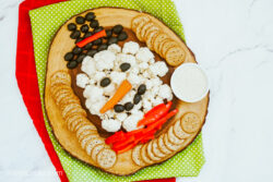 A Snowman Veggie Tray served on a wooden platter with red and green placemats in the background