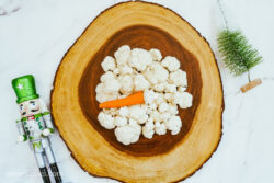 Cauliflower and a carrot on a wooden tray, sitting on a marble countertop