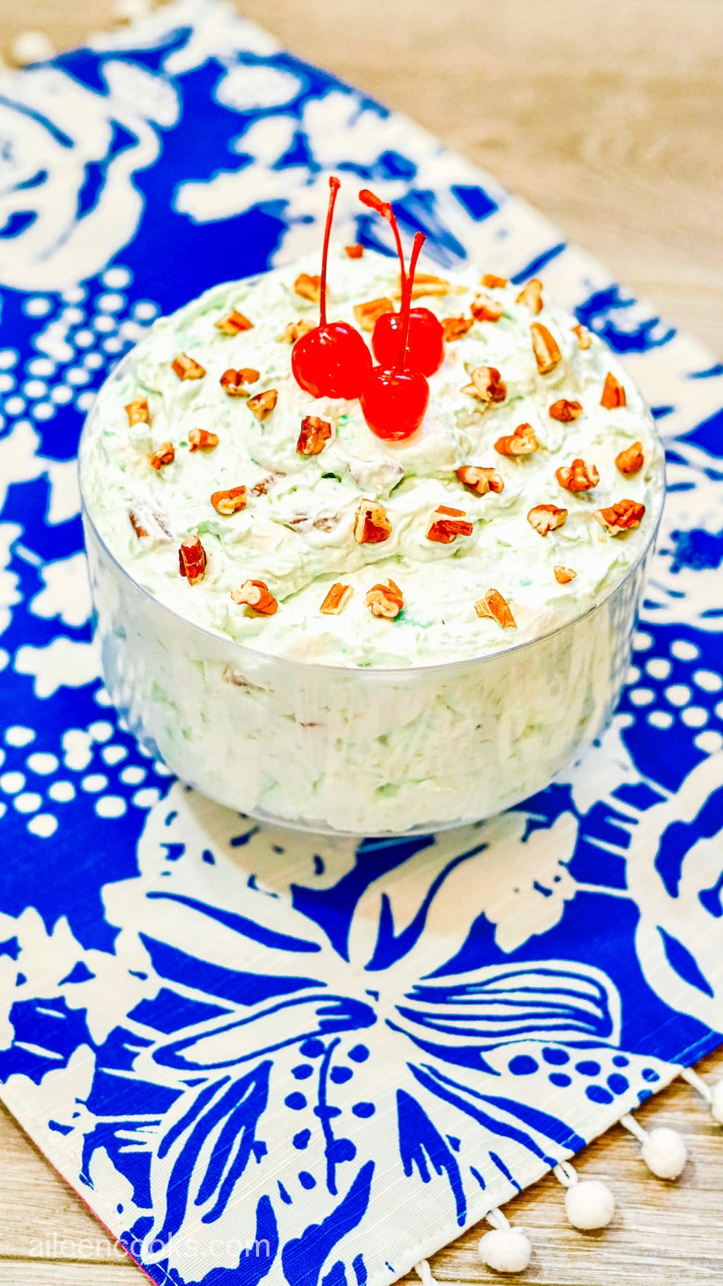 A serving of Watergate Salad in a large glass bowl on top of a blue patterned tea towel