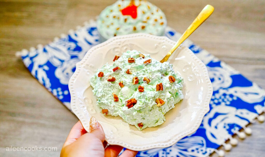 A hand holding up a bowl of Pistachio Pudding Salad with a gold spoon