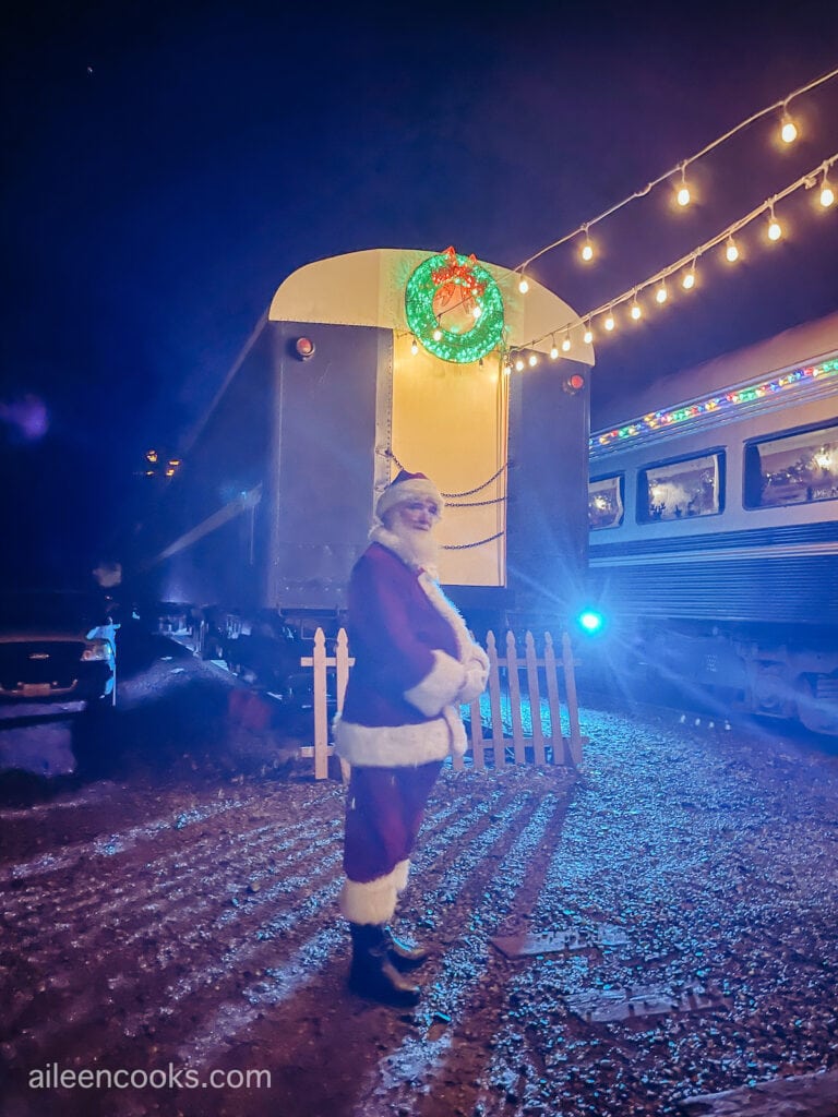 Santa Clause standing outside the evening, in front of a train.
