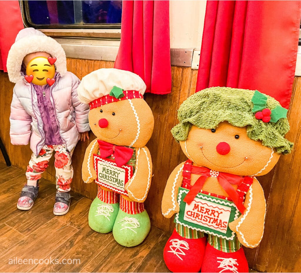 A small child standing next to do large stuffed gingerbread people.