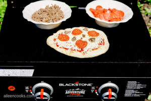 Placing a naan bread pizza on a Blackstone Grill, ready to be grilled to perfection