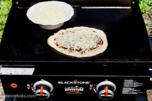 Adding cheese on Flatbread Pizza, sitting on a Blackstone Grill