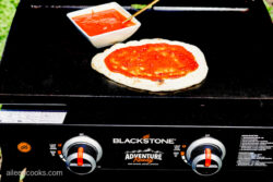 Adding pizza sauce on naan bread, sitting on a Blackstone Grill