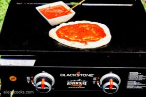 Adding pizza sauce on naan bread, sitting on a Blackstone Grill