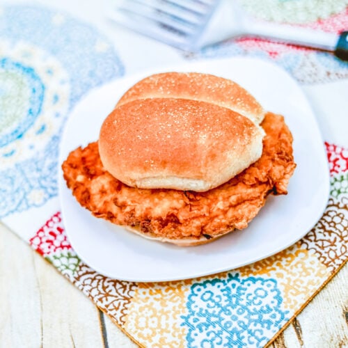 A Crispy Chicken Sandwich, sitting on a white plate, on colorful place mats, ready to be served.