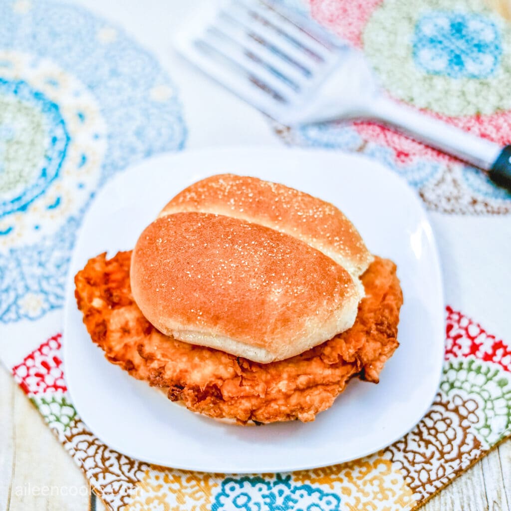 Aerial shot of a Crispy Chicken Sandwich, served on a white plate on a wooden table with patterned place mats.