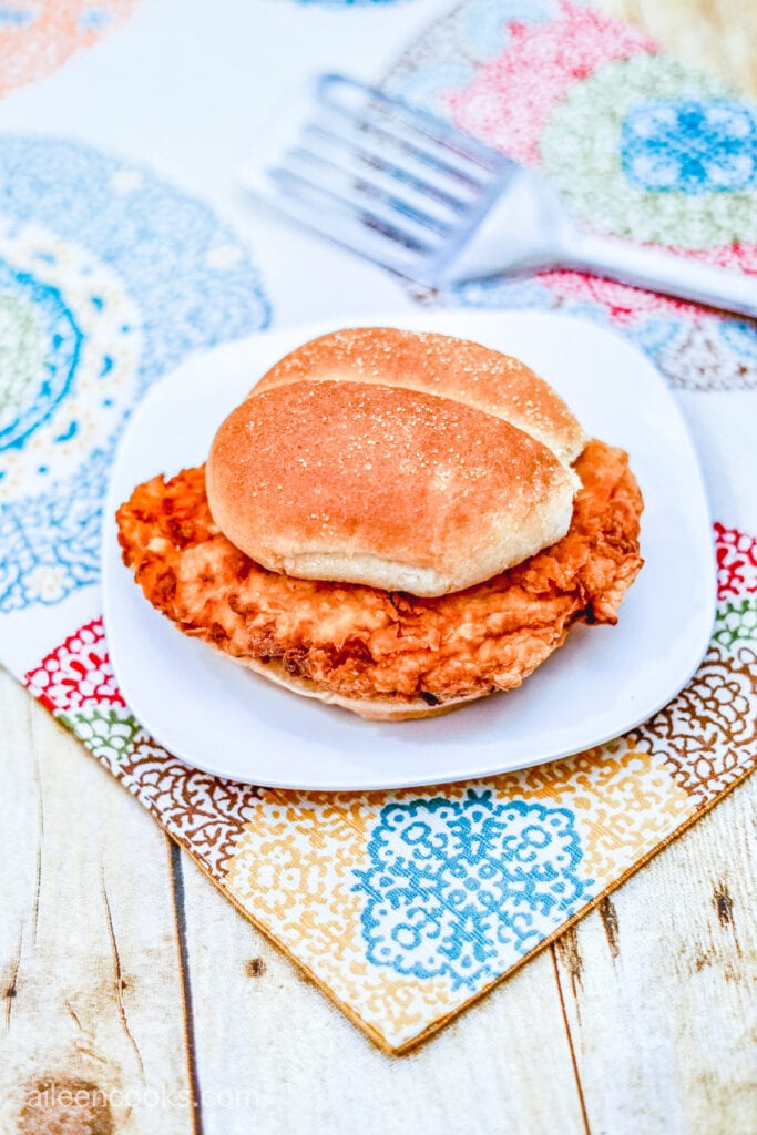 Aerial shot of a Crispy Chicken Sandwich, served on a white plate on a wooden table with patterned place mats.