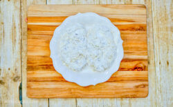 Two pieces of chicken breast coated with flour, sitting on a white plate.