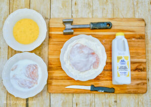 Coating a large piece of raw chicken breast in buttermilk, followed by flour