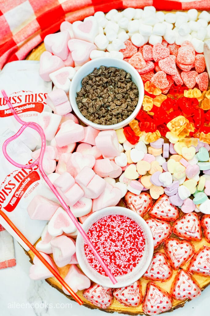 Close up of hot chocolate charcuterie board featuring heart shaped marshmallows, chocolate chips, and sprinkles.