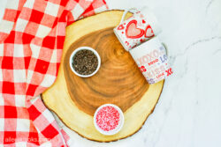 A wood slab with a small bowl of mini chocolate chips and a small bowl of red and pink sprinkles.