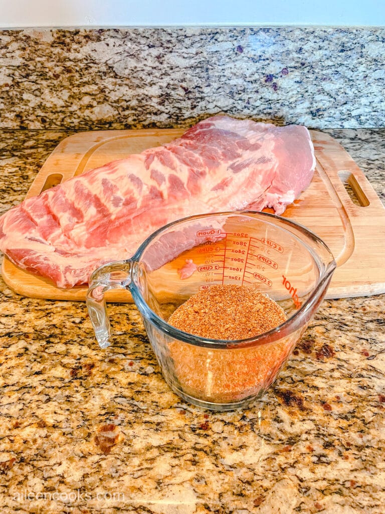 A glass measuring cup full of a seasoning blend in front of a rack of ribs.