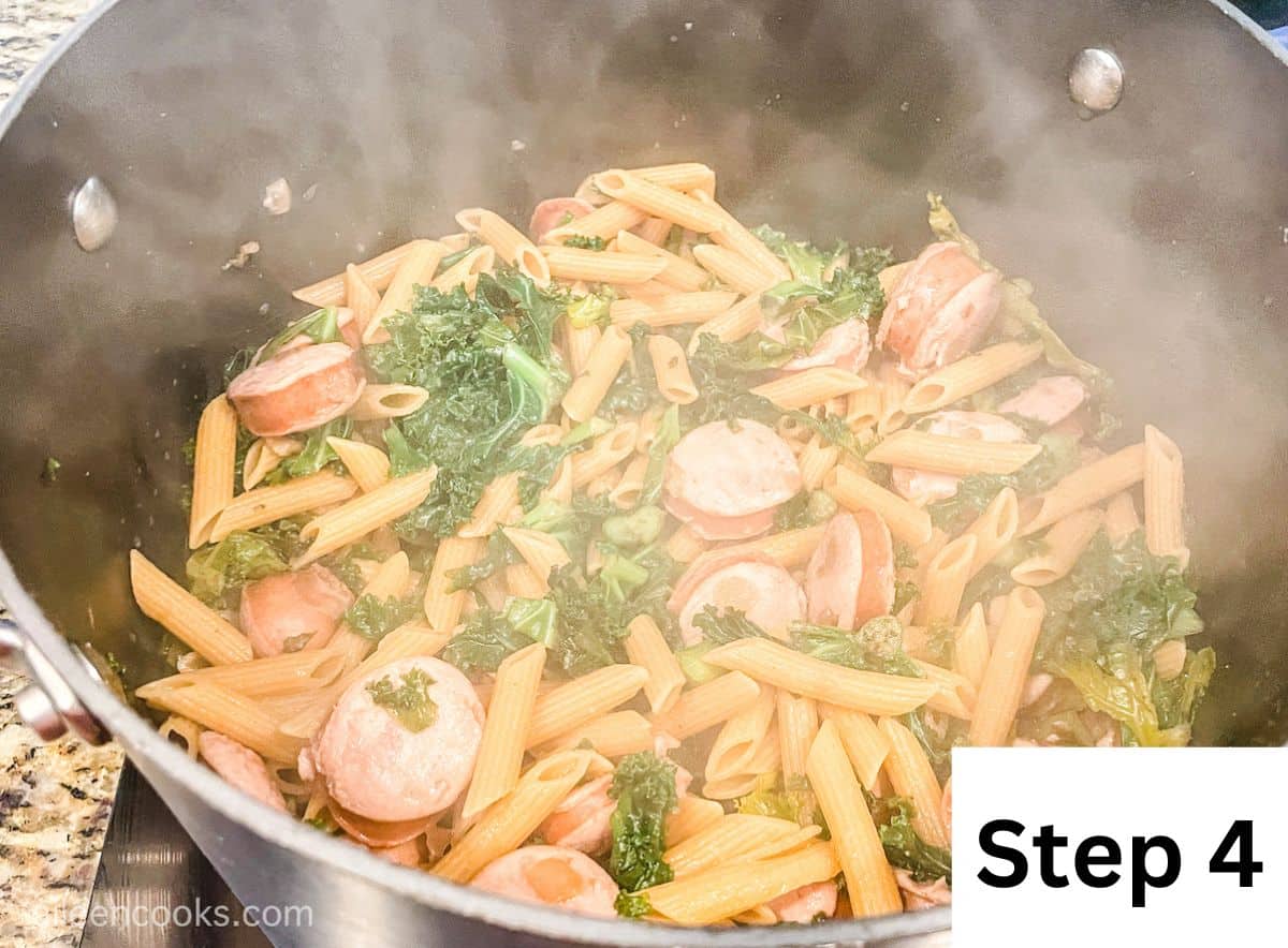 A pot full of cooked pasta, smoked sausage, and kale with steam coming up.