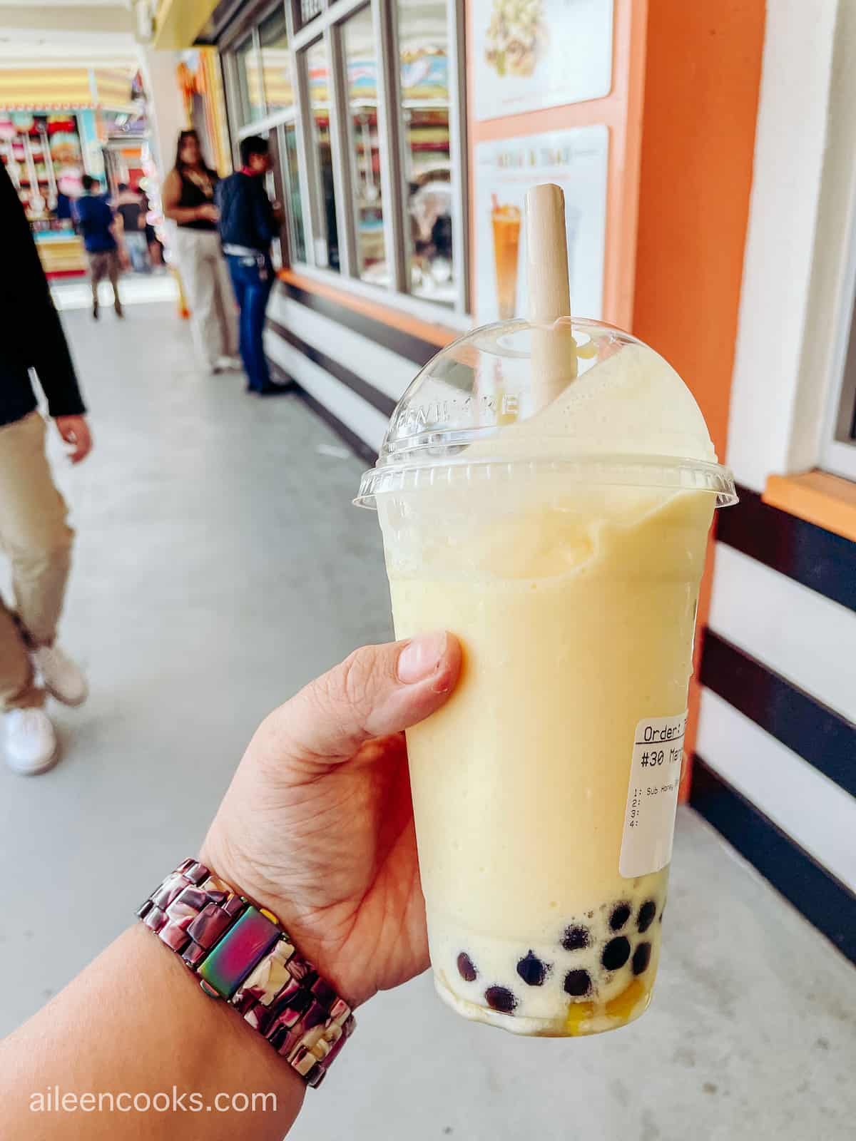 A hand holding a yellow smoothie with boba at the bottom.