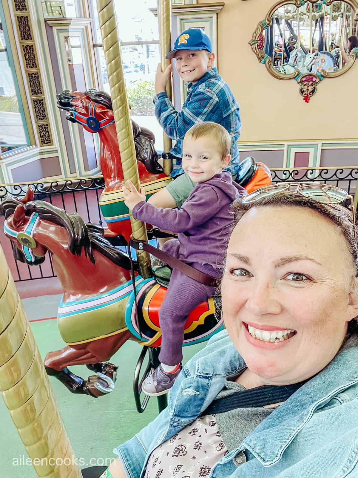 A women on a carousel with a toddler girl and young boy.